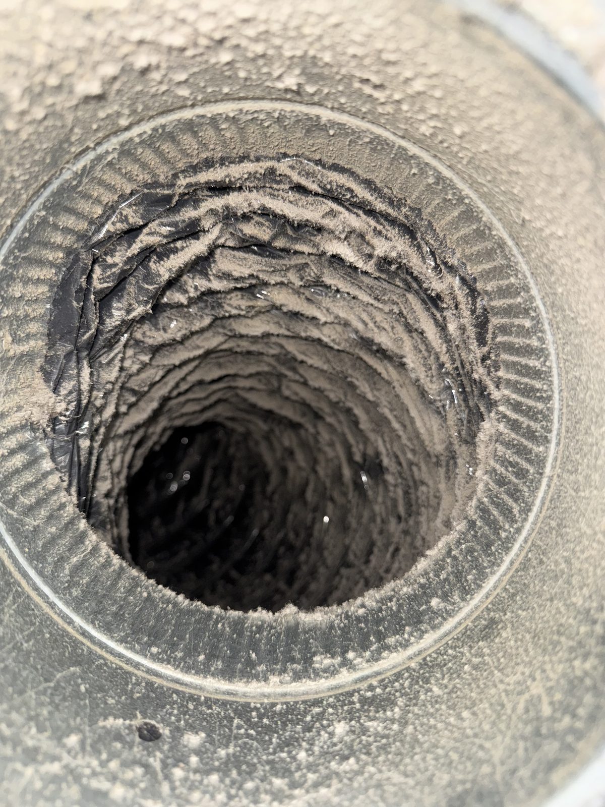 Inside of a flexible air duct before cleaning, coated in grey dust and debris