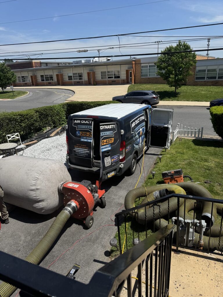 Two branded Air Duct Dynasty vans with collection bag and vacuum hoses set up at a commercial building