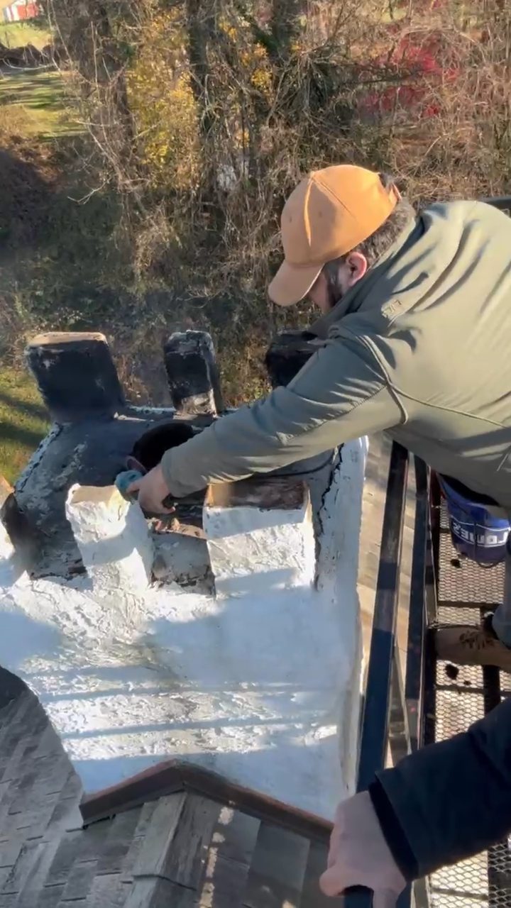 Technician working on a chimney from a lift with autumn trees behind